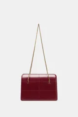 Bolso de hombro de formato rígido en piel color borgoña, con detalle de pespuntes que crean un patrón de cuadrícula. Posee triple compartimento y doble asa de hombro en cadena metálica dorada.