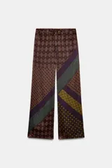 Pantalón de tiro alto confeccionado en seda, con cintura ajustable mediante cordones. Presenta un diseño de patchwork con diversos estampados geométricos y paisley en tonos tierra, verde y violeta.