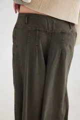 Pantalón de jean con diseño de tiro medio-bajo y piernas anchas. Presenta una pretina ancha con cierre de tres botones metálicos frontales, pinzas decorativas en la cintura y bolsillos delanteros funcionales.