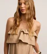 Vestido largo color beige, estilo evasé, confeccionado en tricolina de algodón. Presenta escote hombro a hombro con un volante superpuesto y bajo fruncido.