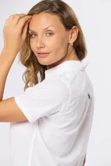 Camisa de lino de manga corta con cuello camisero, cierre frontal de medio botón con botones metálicos personalizados y dos bolsillos en el pecho.