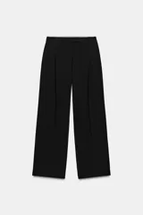 Pantalón negro de tiro alto con pinzas delanteras, bolsillos frontales y falsos bolsillos con solapa en la espalda. Tiene pernera ancha y cierre frontal con cremallera, botón interior y gancho.