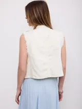 Chaleco vaquero blanco de estilo militar, con doble botonadura frontal de botones oscuros y diseño sin mangas con bordes deshilachados.