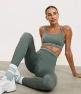 Legging deportiva color verde, confeccionada en poliamida, con cintura baja y rayas horizontales en blanco y gris.