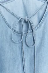 Top de denim celeste, con escote pico, tirantes finos ajustables y detalle de lazada en la espalda. Presenta costuras marcadas en el busto y un calce ligeramente acampanado.