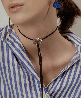 Choker de cinta negra con dije circular central decorado con cristales y tiras colgantes.