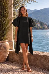 Vestido corto de lino negro con mangas abullonadas y diseño asimétrico con laterales más largos.