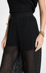 Pantalón calado negro de Le Lis Blanc, con tejido de punto transparente, corte ancho y cintura asimétrica con superposición frontal.