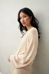 Sweater de punto color beige claro, con cuello redondo y manga larga, decorado con perlas aplicadas en patrón de rombos.