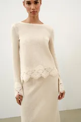 Top de tejido rústico color beige con cuello redondo y mangas largas, con aplicación de crochet a tono en los puños y el ruedo.