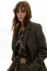 Chaqueta de doble botonadura con diseño de cuadros en tonos verde oscuro y líneas rojizas. Presenta solapas clásicas, bolsillos frontales tipo plaqué, tajo en la espalda y botones de cuero.