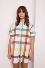 Vestido corto de corte recto y holgado, con mangas cortas y cuello redondo. Presenta un estampado de cuadros grandes en tonos pasteles sobre fondo crema.