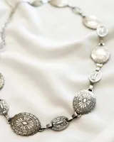 Cinturón plateado con eslabones y apliques ovalados y circulares con diseño labrado.