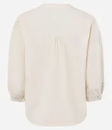 Blusa estilo bata color blanco roto, confeccionada en cambraia de algodón y lino. Presenta cuello con lazo ajustable, canesú fruncido en el busto y mangas tres cuartos con puños elásticos y bordados.