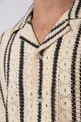 Camisa de manga corta tejida al crochet con diseño de rayas verticales negras sobre una base color crudo. Presenta cuello solapa y cierre frontal con botones.