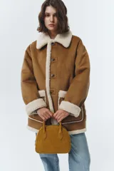 Chaqueta reversible de cuero sintético color marrón con forro de corderito sintético blanco. Presenta cuello de solapa, cierre frontal con botones, bolsillos de parche y detalles de corderito en puños, bolsillos y bordes.