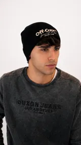 Gorro tipo beanie de punto acanalado en color negro, con bordado frontal en color crema que incluye la frase 'Off-Court' y detalles de marca.