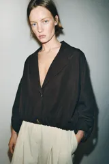 Blazer corto de color marrón oscuro, con cuello solapa, cierre frontal de botones y mangas largas con puños vueltos. Presenta un diseño con bajo elástico que le otorga una silueta ajustada en la cintura.