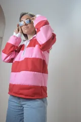 Sweater estilo rugby a rayas horizontales rosas y rojas con cuello blanco y cierre parcial con botones.