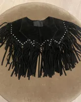 Chaleco corto de cuero azul marino, estilo western, con cuello solapa y profusión de flecos largos en todo el contorno. Presenta detalles de tachas metálicas plateadas a lo largo del borde del cuello y los hombros.