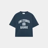Camiseta azul con estampado frontal que incluye el texto "EME STUDIOS" y "BADGE" en color blanco.