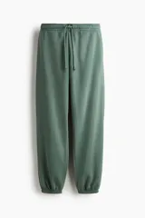 Pantalón de jogging verde con interior cepillado suave, cintura elástica fruncida con cordón ajustable, bolsillos laterales discretos y elástico revestido en los bajos.