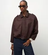 Campera bomber de gamuza sintética color marrón oscuro, con cuello clásico, cierre frontal, hombros caídos y puños ajustados. Presenta un diseño holgado con textura aterciopelada.