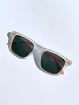 Lentes de sol con armazón de acetato traslúcido en acabado mate y cristales polarizados con efecto espejado en tono naranja. Presentan detalles en color naranja en las patillas y el frente.