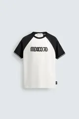 Camiseta de corte regular con diseño color block, cuerpo en color blanco y mangas ranglán en color negro. Presenta cuello redondo, detalles de rib a contraste en los puños y estampado frontal con la leyenda Mexico 70.