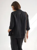 Camisa blanca de lino con cuello clásico, mangas largas y cierre frontal con botones color madera. Presenta detalles de frunces verticales en el frente.