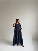 Vestido largo azul oscuro con diseño asimétrico que combina un lado liso con un lado estampado de hojas, manga corta y bolsillo frontal aplicado.