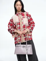 Camisa de corte oversize con estampado de cuadros en tonos rojos, blancos y negros. Presenta un diseño de estilo patchwork con parches de tela texturizada en color beige en el pecho y a lo largo de la botonera. Cuenta con cuello clásico, mangas largas y bordes deshilachados que le otorgan un aspecto desgastado y moderno.