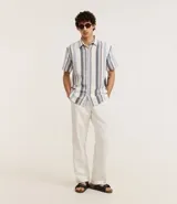Camisa de hombre de manga corta con cuello tradicional y abotonado frontal. Presenta un tejido texturizado con un patrón de rayas verticales en tonos beige, blanco y marrón claro.
