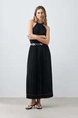 Vestido largo negro plisado con cuello halter y cinturón plateado.