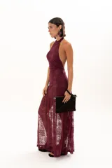Vestido largo de encaje color bordó, con escote halter y diseño ajustado en el torso que se extiende hasta la cintura, donde continúa con una falda larga de encaje transparente.