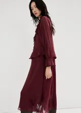 Vestido largo bordó de poliéster, de corte oversize, con escote en V y detalle de volantes en la cintura y el canesú. Cuenta con mangas largas y forro interior.