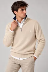 Buzo de tejido fino color beige con medio cierre frontal y cuello alto, de manga larga con puños y ruedo elásticos estriados. Incluye detalle bordado pequeño en el pecho.