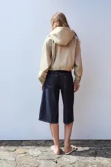 Cazadora color beige con capucha ajustable, manga larga con puño elástico, bolsillos frontales con solapa, bajo ajustable y cierre frontal con cremallera y botones a presión.