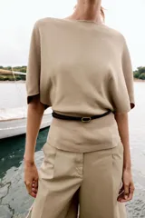 Top de punto color beige con cuello barco y mangas cortas anchas tipo murciélago. Cuenta con cintura entallada con ribete elástico y un cinturón fino de cuero sintético marrón con hebilla metálica dorada.