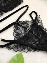 Conjunto de lencería compuesto por un bralette de encaje negro con cierre frontal de gancho y breteles regulables, y una tanga de encaje con tiras elásticas laterales ajustables y argollas metálicas.