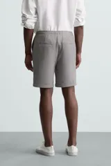 Bermuda negra de corte recto, con cintura elástica ajustable mediante cordón, pliegues frontales y bolsillos de vivo en la espalda. El bajo tiene un dobladillo vuelto.