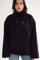 Abrigo negro de paño con diseño cruzado, cuello alto y cierre frontal con botones. Presenta una silueta estructurada y bolsillos laterales.
