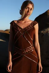 Vestido midi de gamuza color marrón cognac, con escote en V y detalles de calados geométricos artesanales en rombos. Presenta costuras decorativas con ribetes de cuero metalizado en tono cobre.