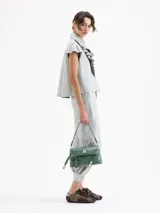 Camisa de cuero ovino color gris claro, con cuello camisero, volados centrales y mangas cortas con volumen generado por frunces en la copa. Cierre frontal con broches forrados.