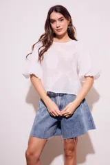 Blusa blanca traslúcida con estampado floral en relieve, cuello redondo y mangas globo cortas.