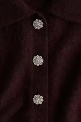 Saco de punto de manga corta color bordó, con cuello camisero y cierre frontal de botones con strass. Presenta terminaciones acanaladas en mangas y ruedo.