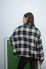 Chaqueta de corte recto con cierre frontal, cuello camisero y diseño a cuadros en tonos negro y beige.