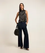 Blusa sin mangas de poliéster satinado color negro con estampado geométrico de líneas blancas y cuello alto drapeado.