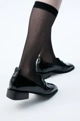 Mocasín de cuero color crema, con punta cuadrada, suela cuadrada negra y tacón bajo.