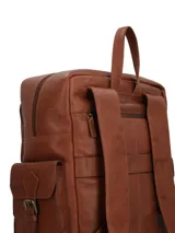 Mochila de cuero natural color marrón, con diseño estructurado. Cuenta con un compartimento superior con cierre, un bolsillo frontal con solapa y hebillas metálicas decorativas, y bolsillos laterales. Presenta un logo grabado en el frente y manija superior.
